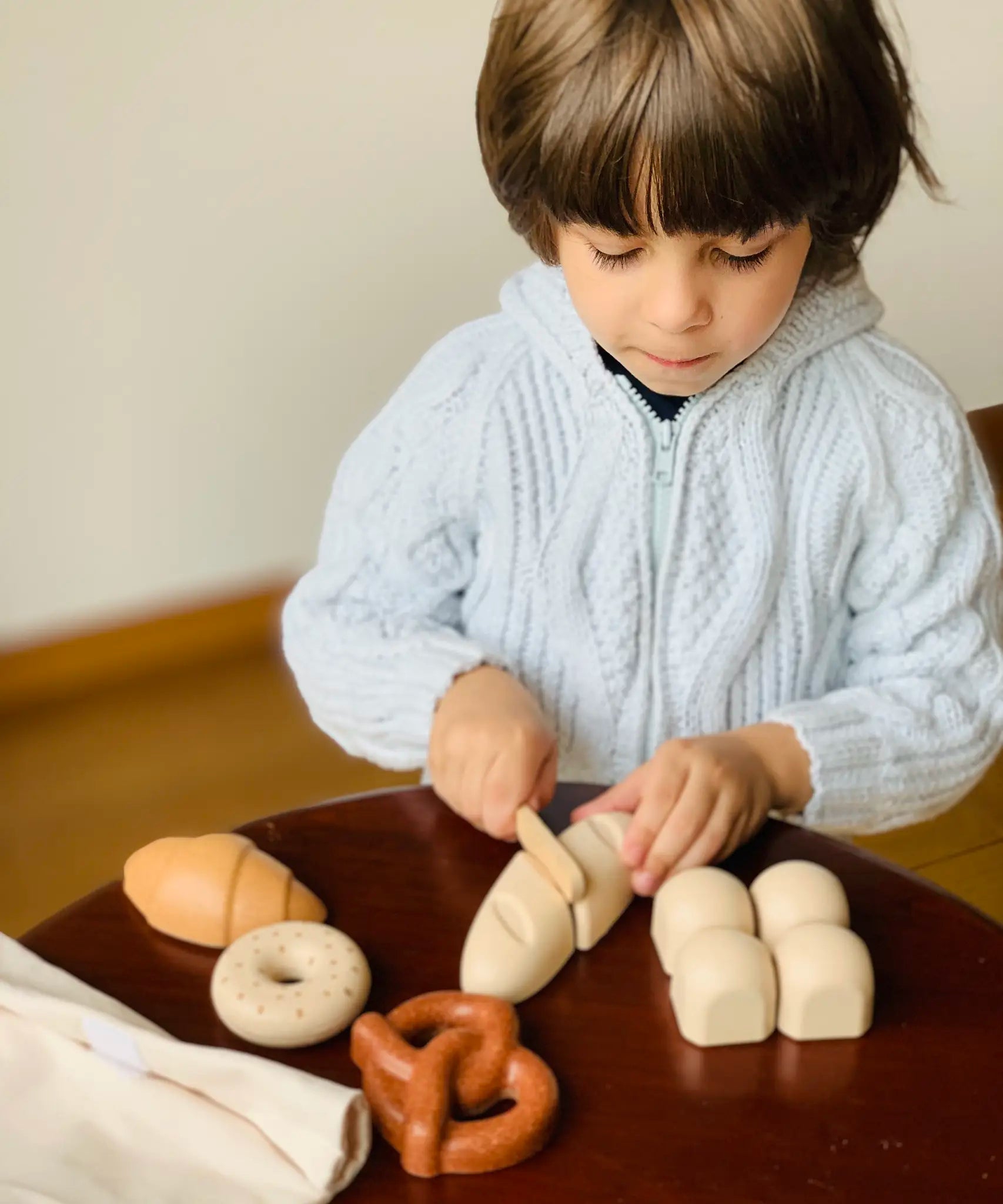 Child holding the wooden knife on a pretend bread roll from the PlanToys bread play set