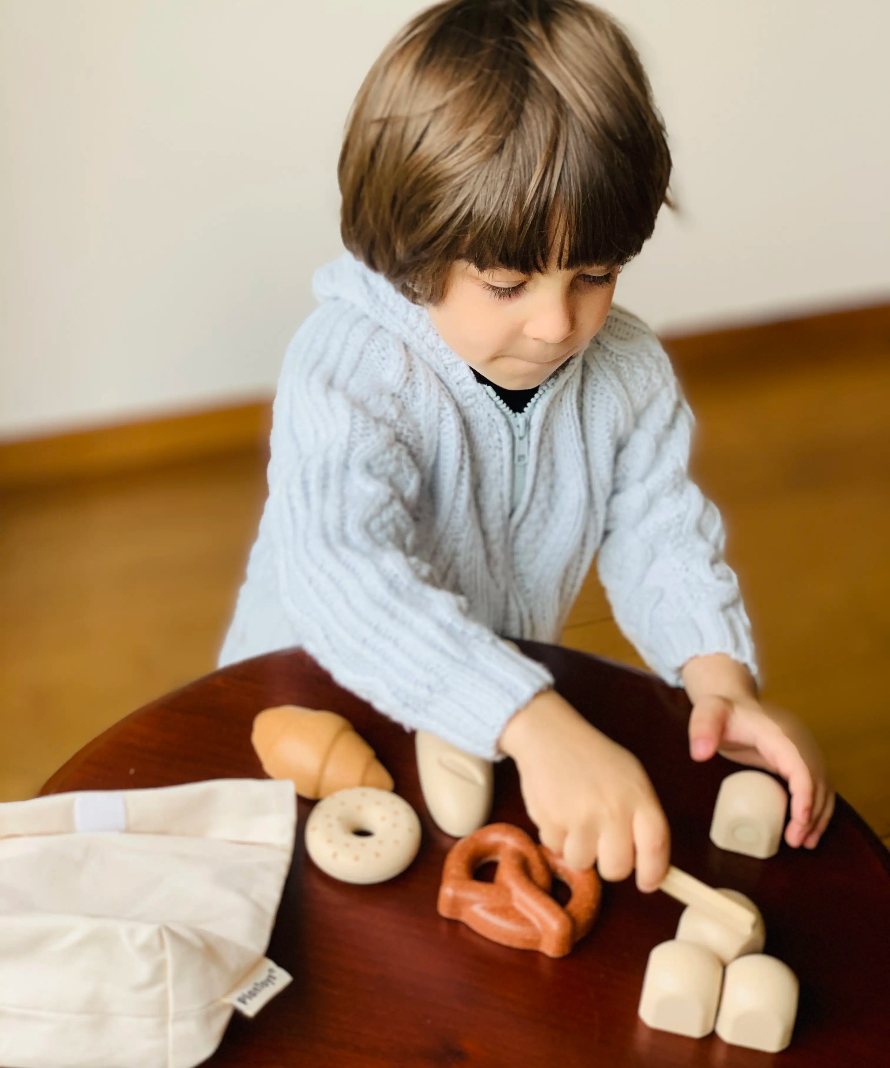 Child playing with pretend rolls from the PlanToys bread play set