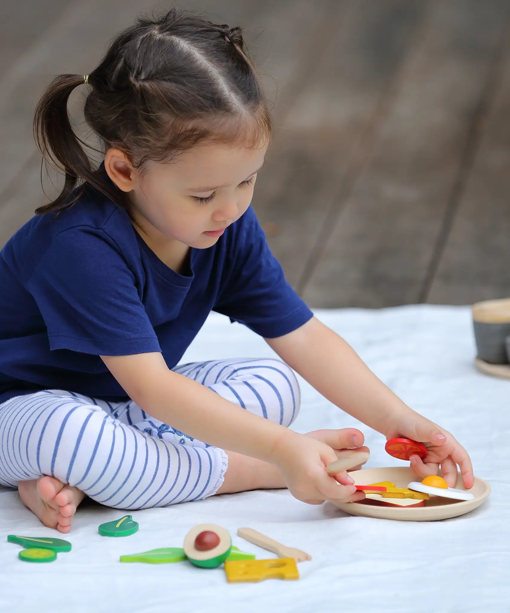 Child making a sandwich from different play food pieces from the Plan Toys breakfast menu play set