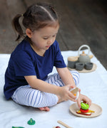 Child making a sandwich from different play food pieces from the PlanToys breakfast menu set