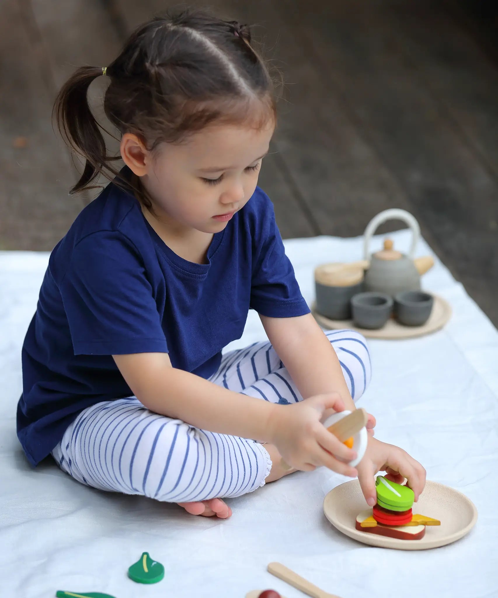 Child making a sandwich from different play food pieces from the PlanToys breakfast menu set