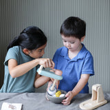 Child holding on a bowl filled with play food and another holding on the mixer from the PlanToys cake mixer set