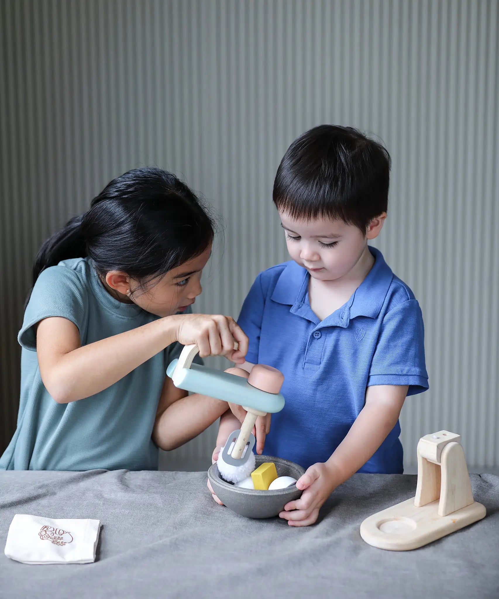 Child holding on a bowl filled with play food and another holding on the mixer from the PlanToys cake mixer set
