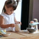 Pieces from the PlanToys cake mixer set on a table with a child opening the cotton bag
