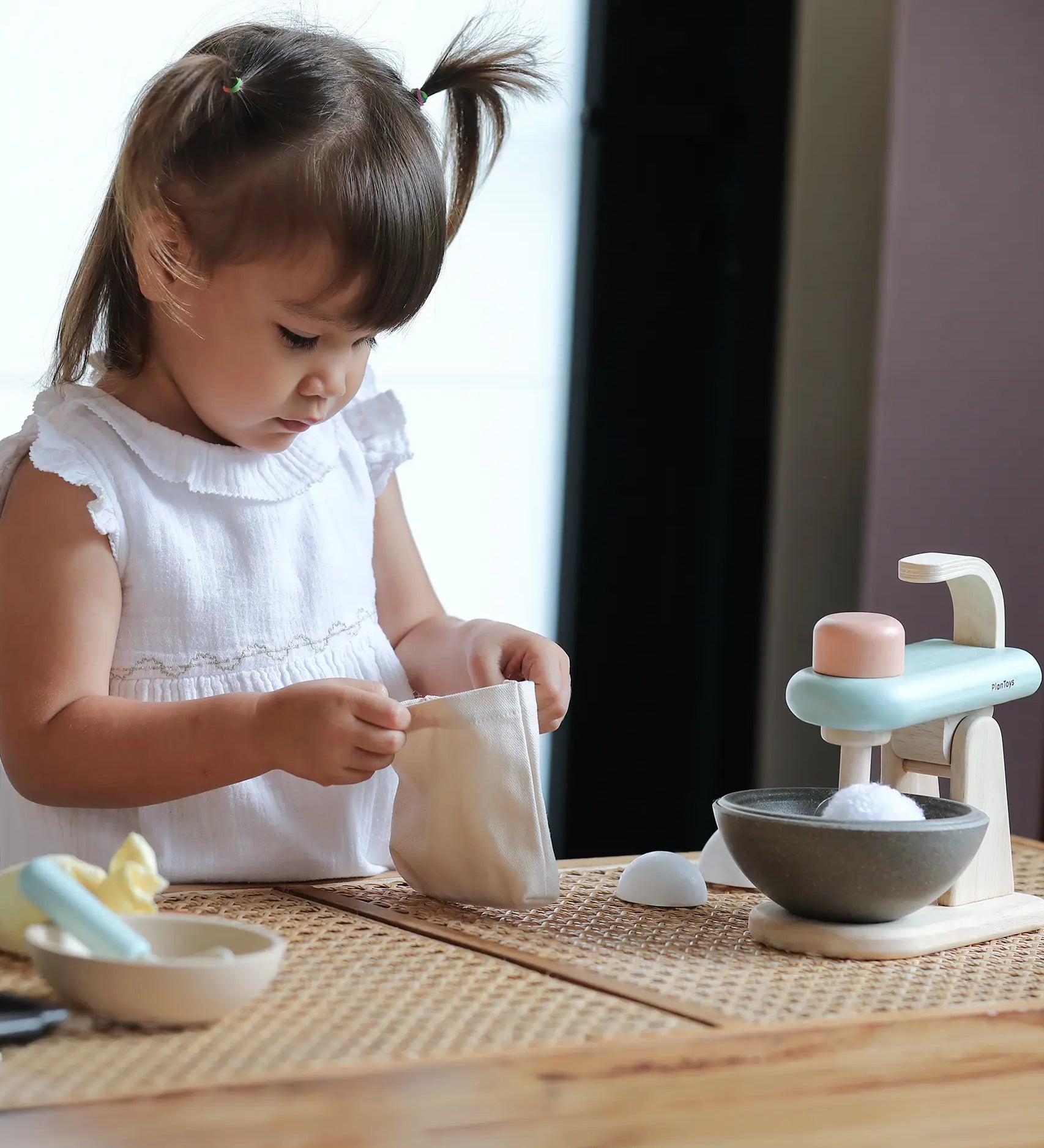 Pieces from the PlanToys cake mixer set on a table with a child opening the cotton bag