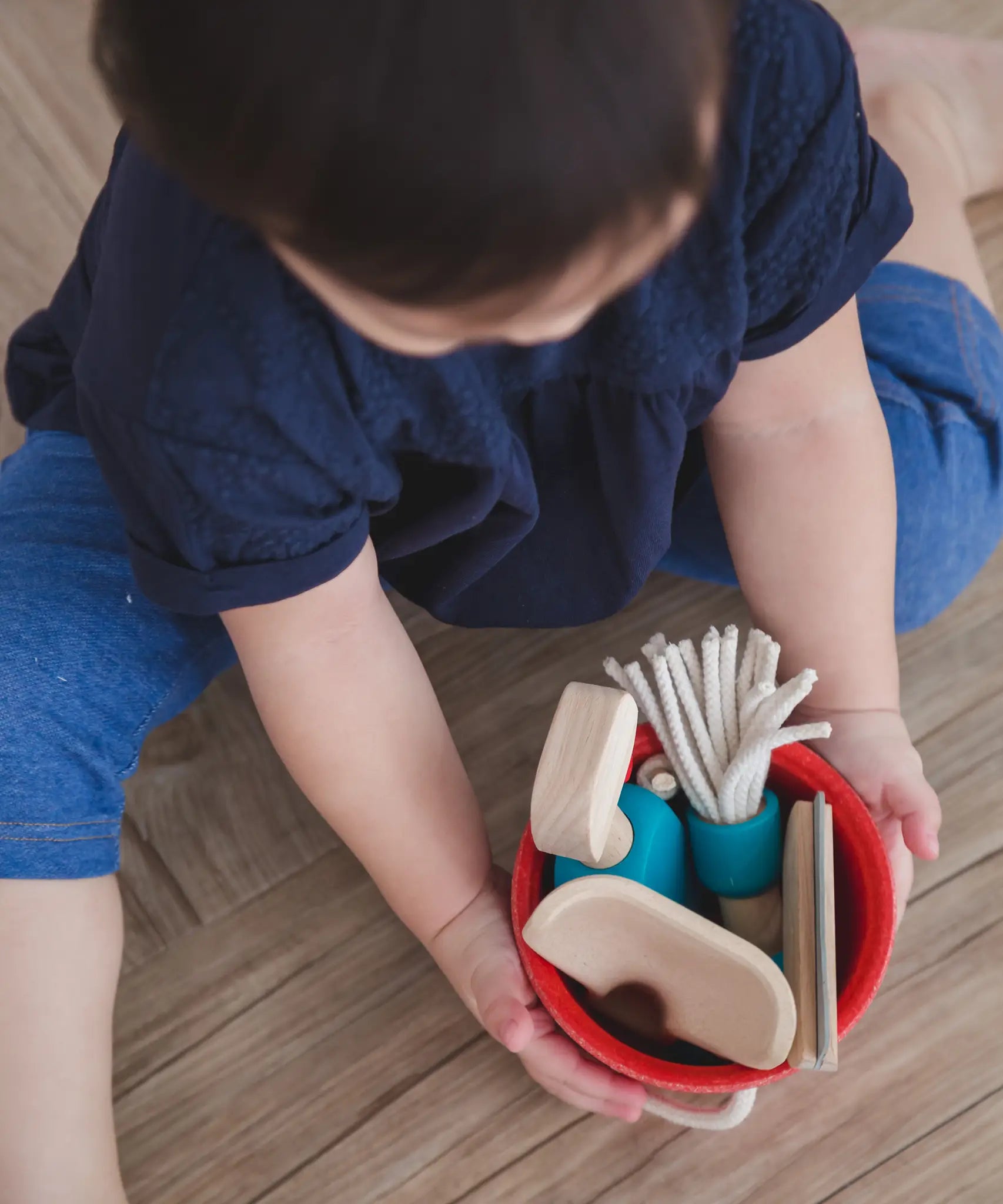 Overhead view of a child holding onto the red bucket from the PlanToys cleaning set filled with tools 