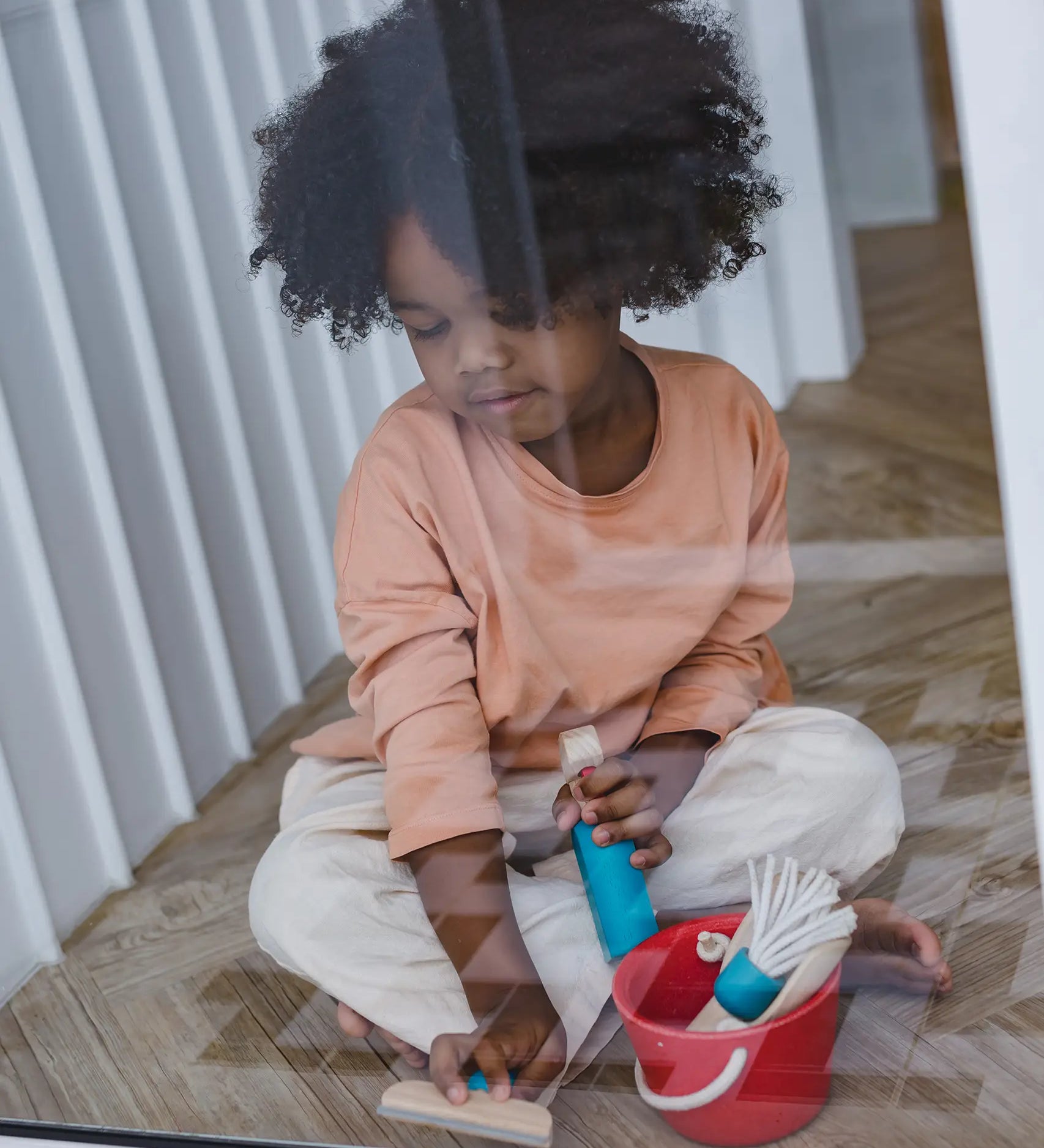Child cleaning a window using the tools from the PlanToys cleaning set