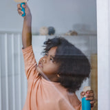 Child holding a window spray bottle and scraper from the PlanToys cleaning set