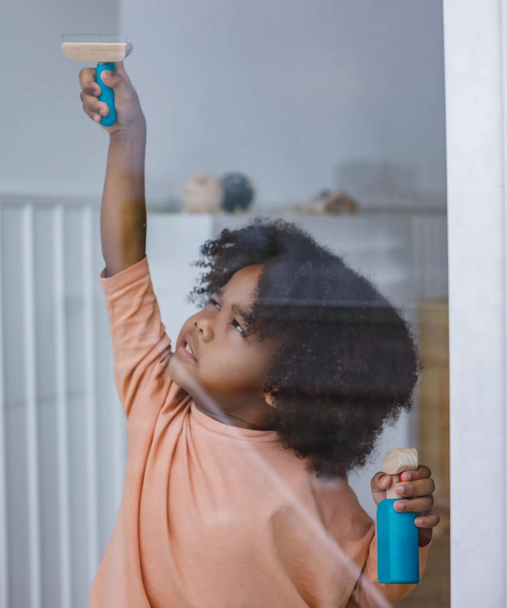 Child holding a window spray bottle and scraper from the PlanToys cleaning set