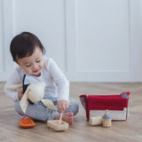 Child reaching into a bowl with a spoon next to a carry bag from the PlanToys feeding set 
