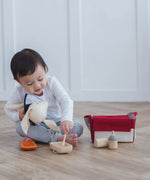 Child reaching into a bowl with a spoon next to a carry bag from the PlanToys feeding set 