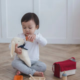 Child feeding a teddy bear with a bottle from the Plan Toys doll feeding set with other accessories on the floor