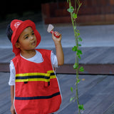 Child wearing the vest and hat from the PlanToys fire fighter set holding a pretend axe next to a vine