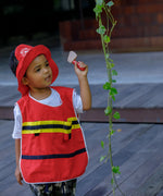 Child wearing the vest and hat from the PlanToys fire fighter set holding a pretend axe next to a vine