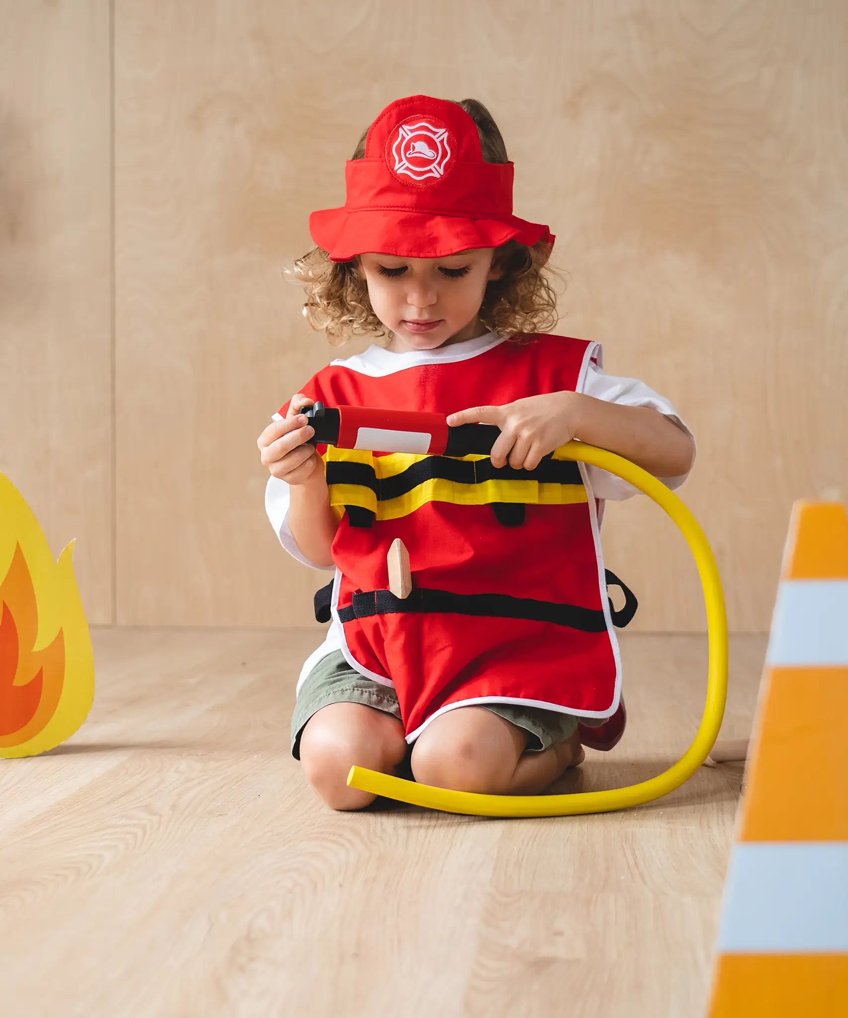 Child holding the hose from the PlanToys fire fighter play set wearing the vest and hat