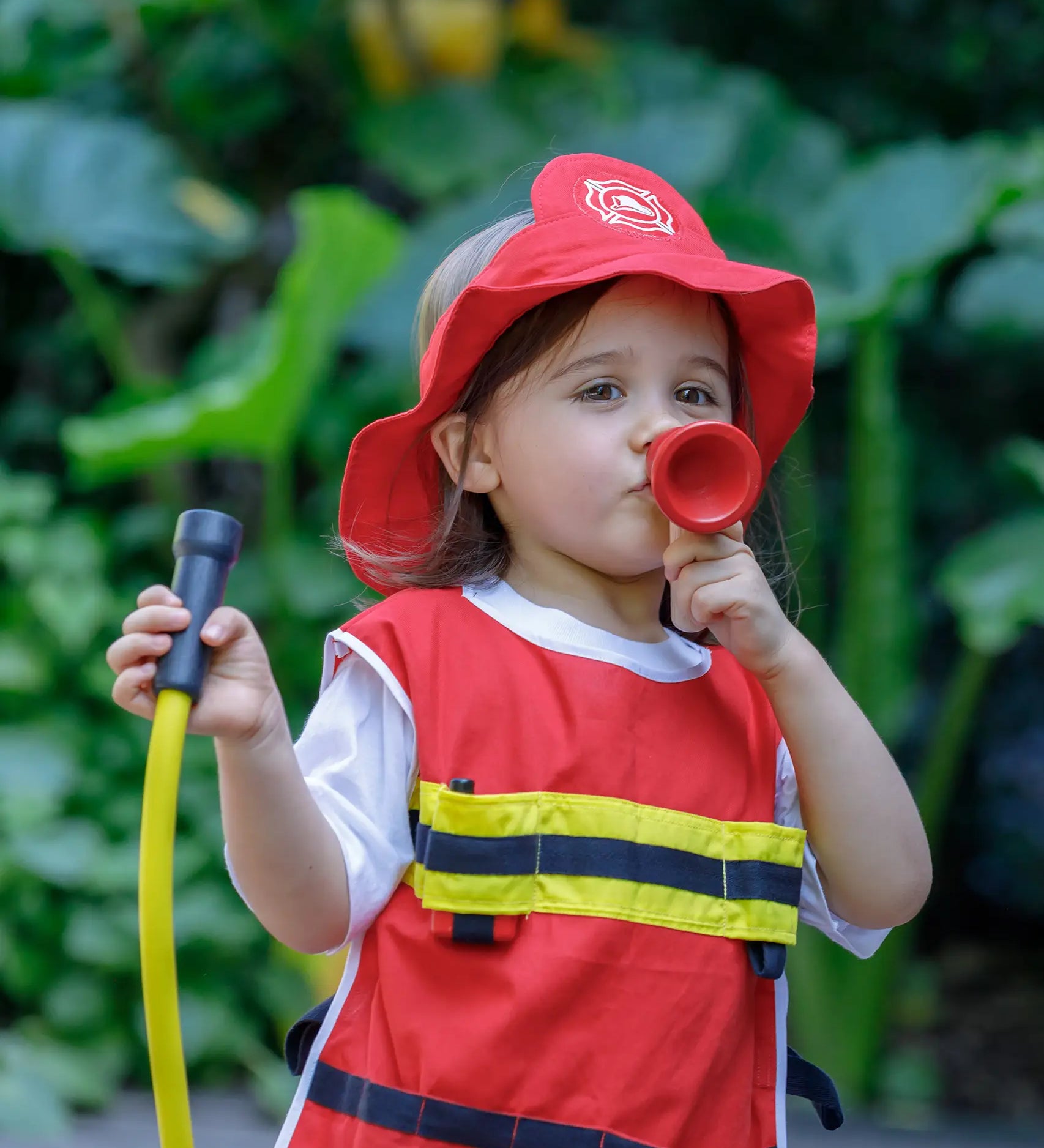 Child playing with the PlanToys fire fighter set wearing the vest, hat and holding the hose and mega phone