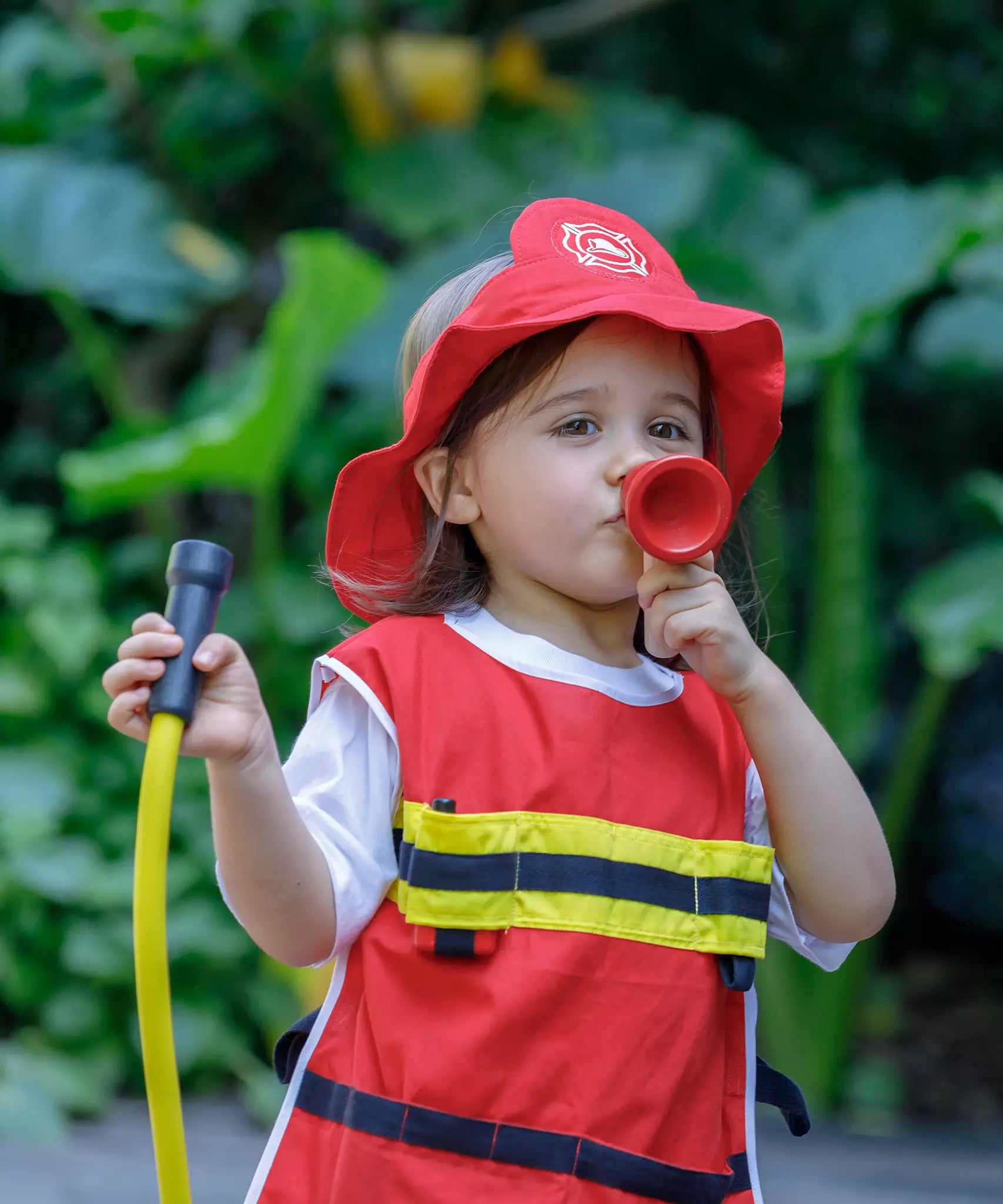 Child playing with the PlanToys fire fighter set wearing the vest, hat and holding the hose and mega phone