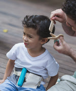 Adult holding a pair of wooden scissors and comb from the PlanToys hair dresser set next to a child's head showing scale