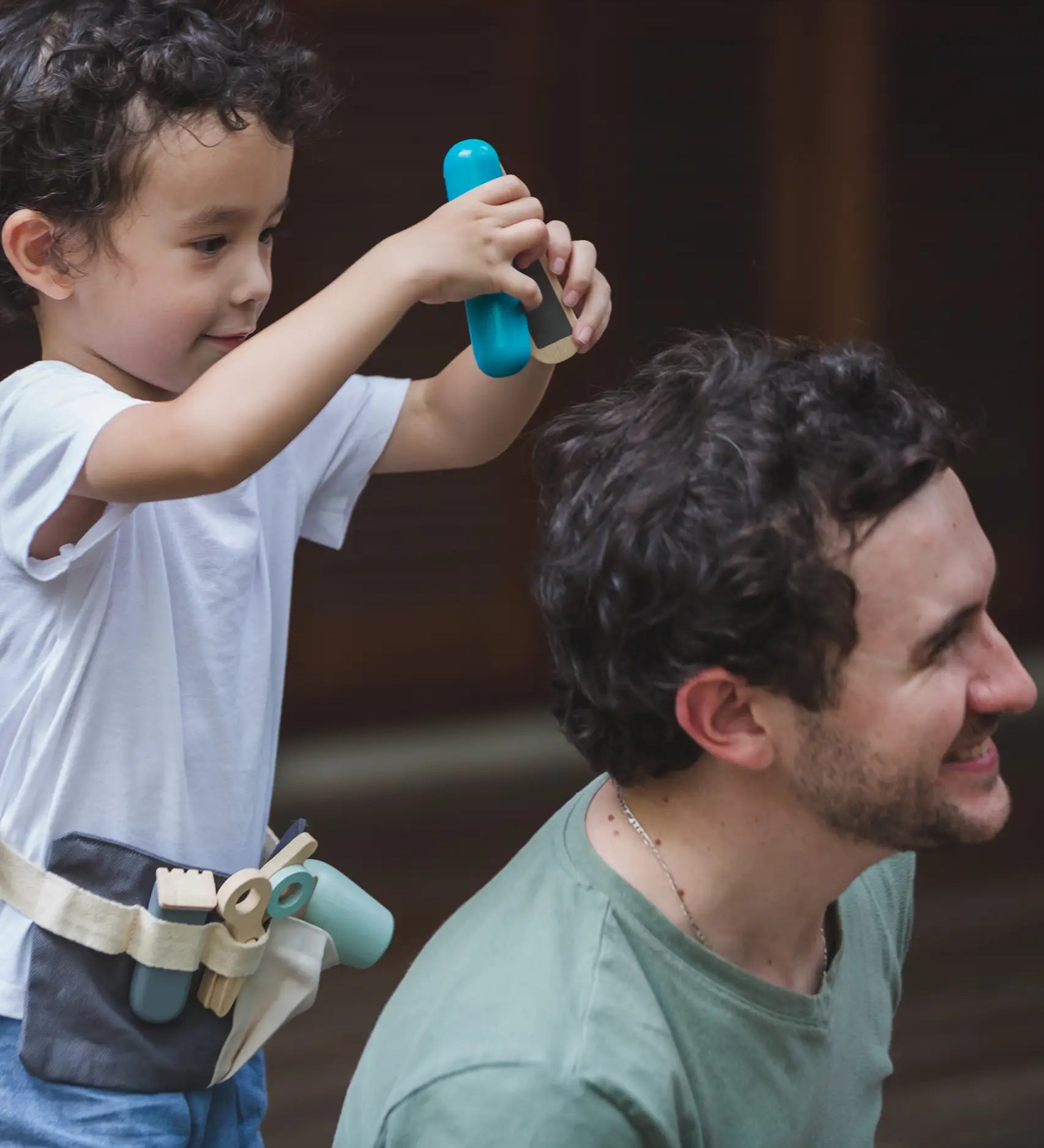 Child with a PlanToys hair dresser set waist bag with accessories and holding hair straighteners. 