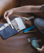 Plan Toys hair dresser waist bag laid flat with a child reaching for a hair brush