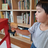 A close up of a child playing with the drill from the Plan Toys wooden handy carpenter set available at Babipur