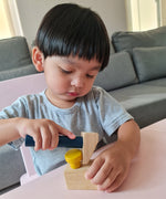 A close up of a child playing with the hammer from the Plan Toys wooden handy carpenter set available at Babipur