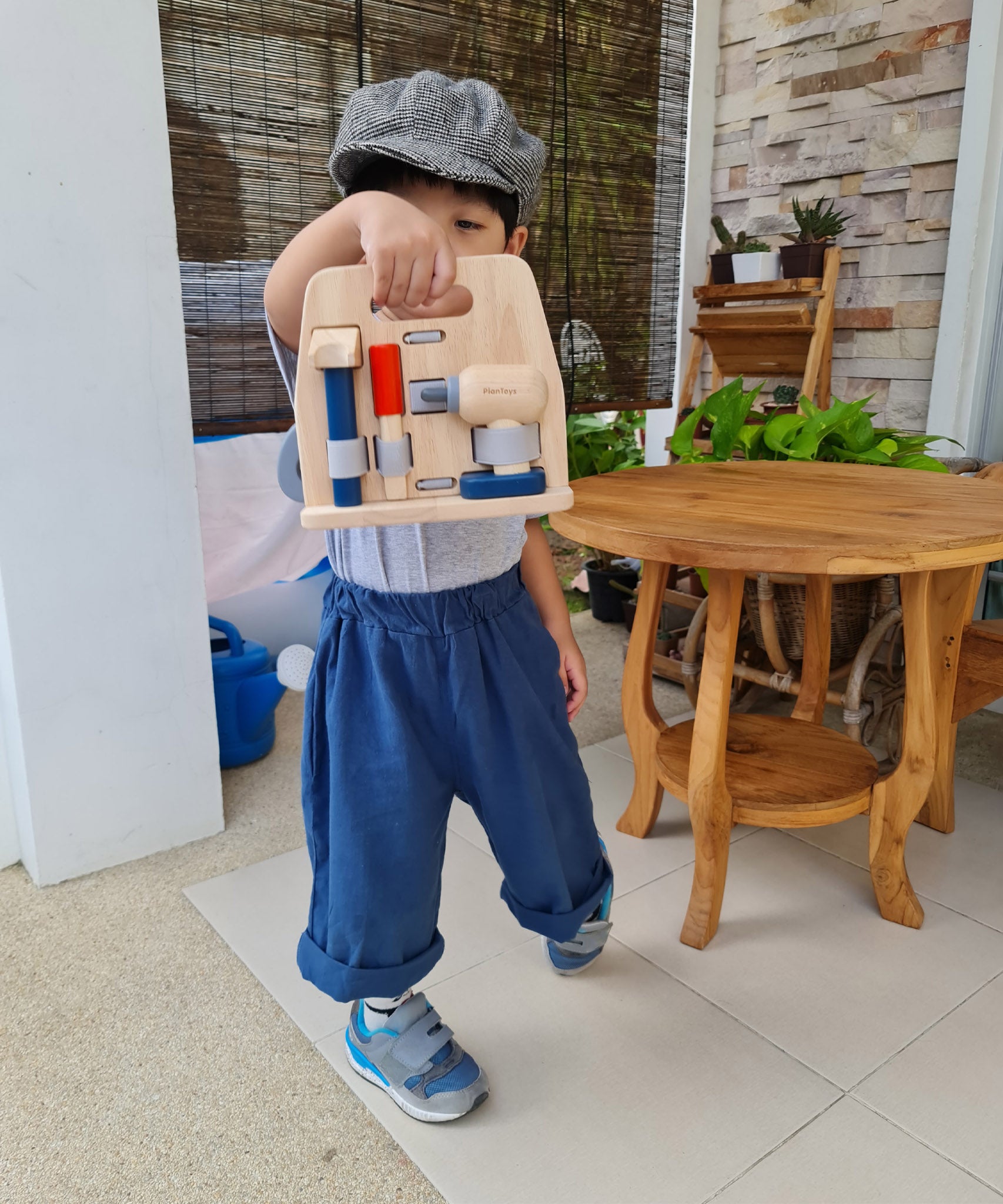 A child holding the Plan Toys wooden handy carpenter set tool stand showing the hammer, chisel and drill. Role play set available at Babipur