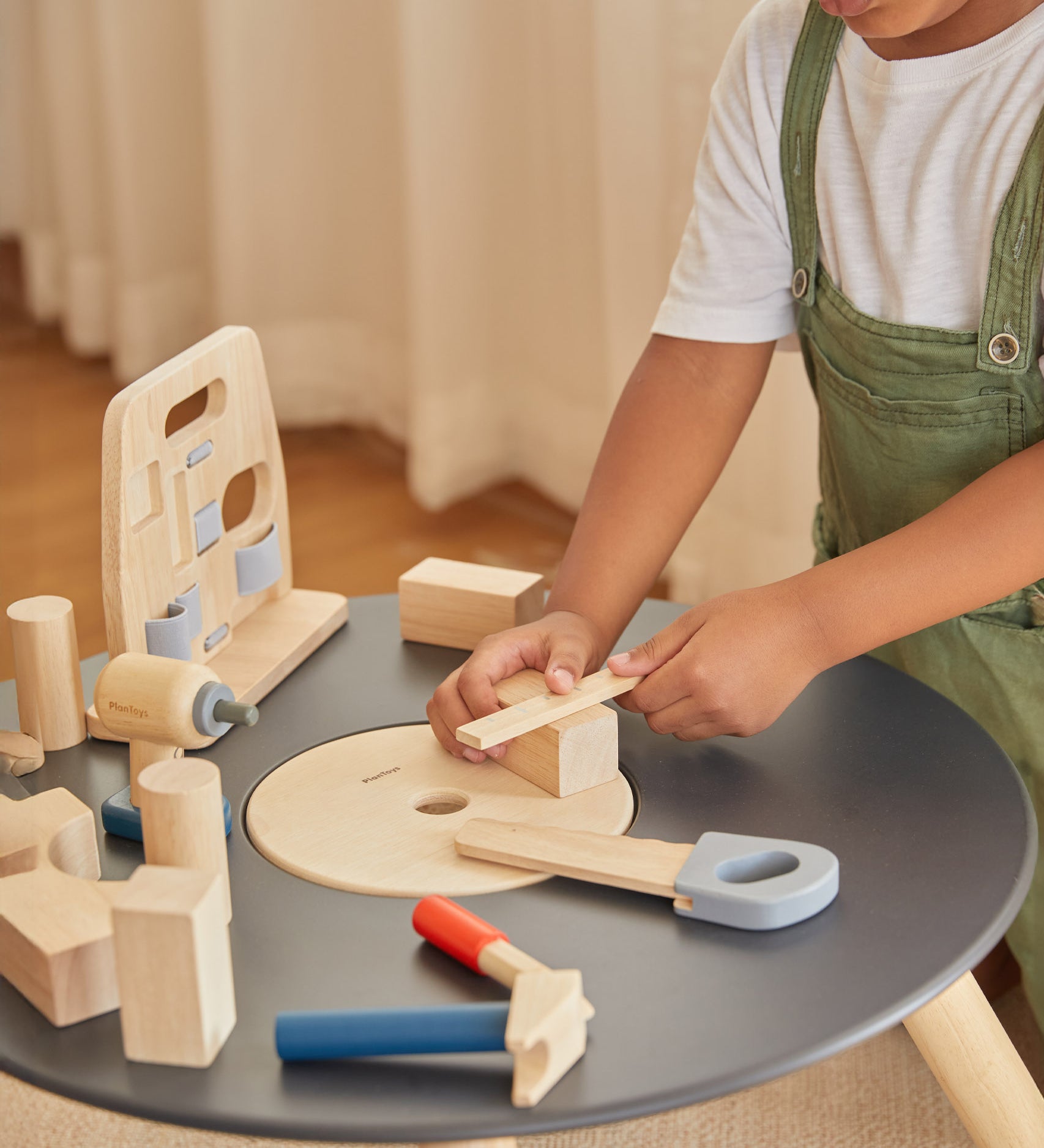 A close up of a child using the ruler from the Plan Toys wooden handy carpenter set available at Babipur with the other tools standing on a wooden Plan Toys table