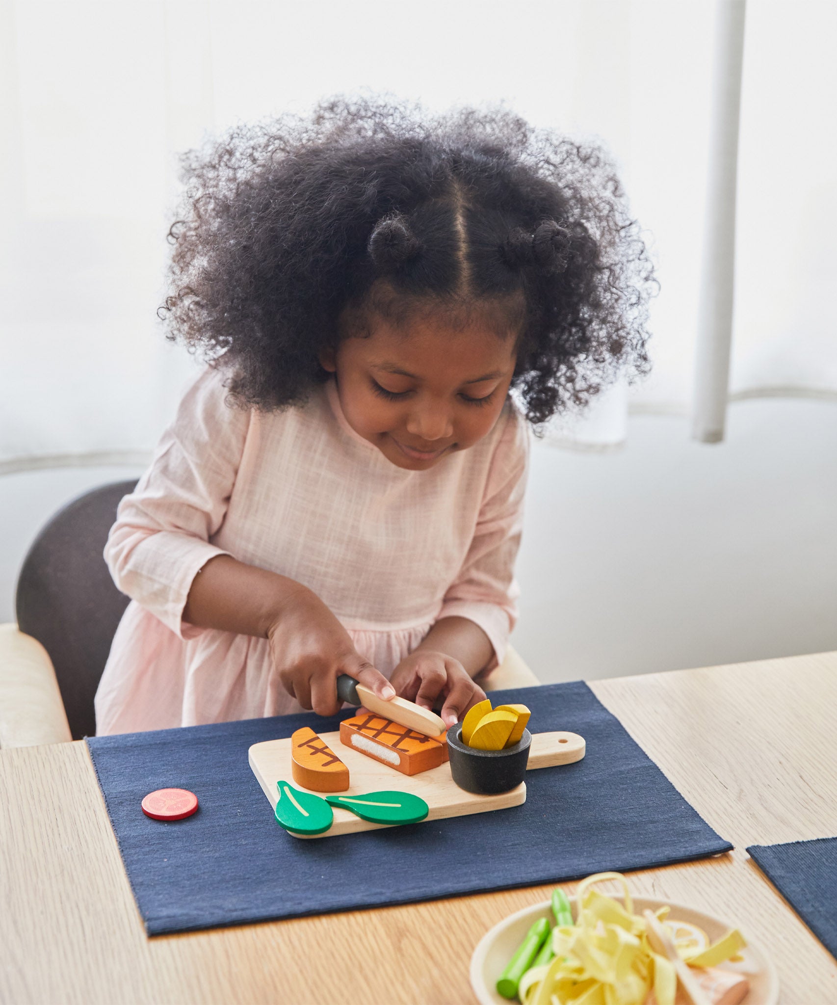 A girl sat by the table and cutting through the steak from the Plan Toys wooden steak set and available at Babipur.