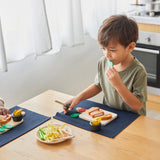 A boy sat by the table and playing with the Plan Toys wooden steak set and available at Babipur.