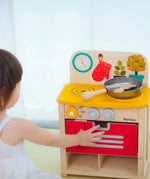 Child closing the oven door on the PlanToys kitchen set