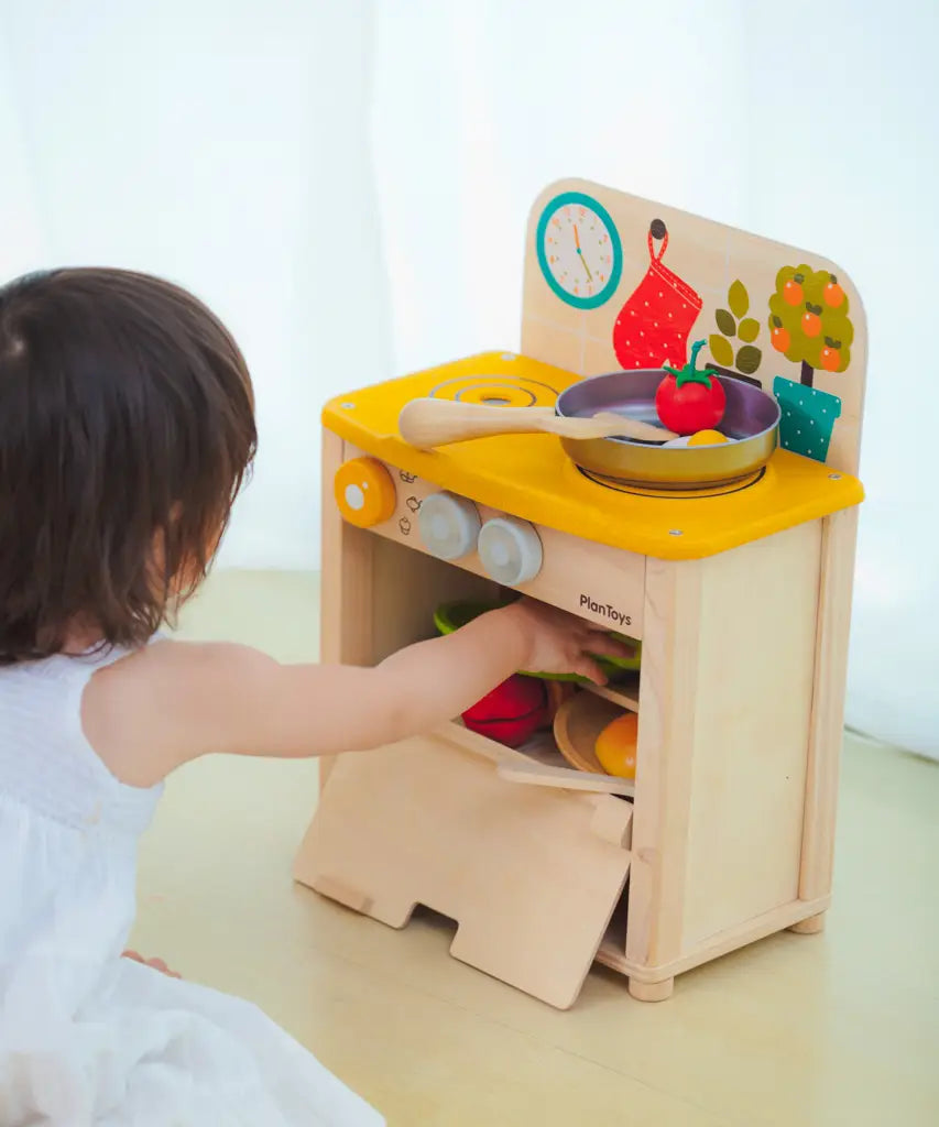 Child reaching into the oven compartment filled with Playfood from the PlanToys kitchen set