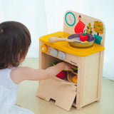 Child reaching into the oven compartment filled with Playfood from the PlanToys kitchen set