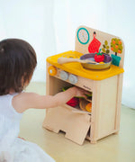 Child reaching into the oven compartment filled with Playfood from the PlanToys kitchen set