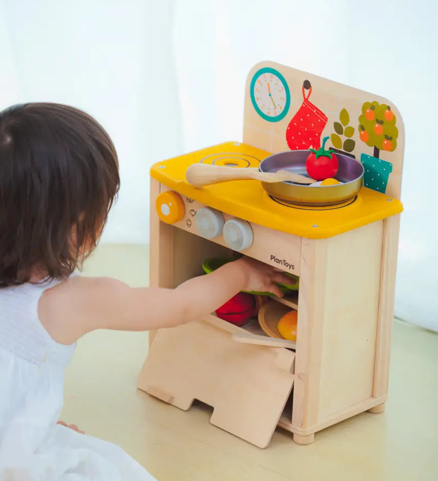 Child reaching into the oven compartment filled with Playfood from the PlanToys kitchen set