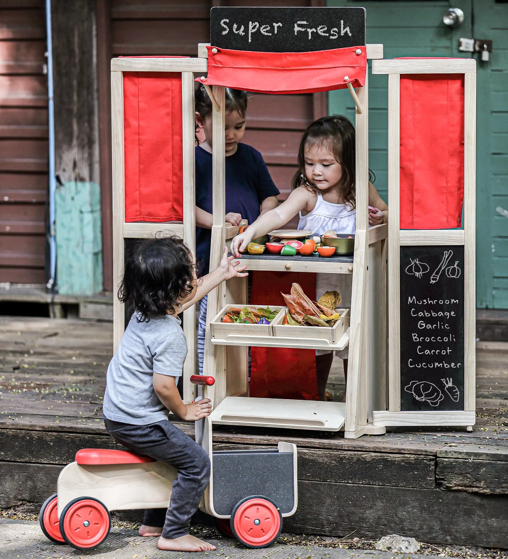 Children playing with the PlanToys play centre made into a fresh market shop. 