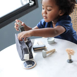 Child putting different accsories from the PlanToys shaving set in a cotton bag.