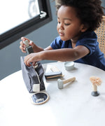 Child putting different accsories from the PlanToys shaving set in a cotton bag.