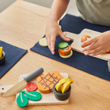 A close up of a child playing with the Plan Toys wooden steak set on the table. Set is available at Babipur.