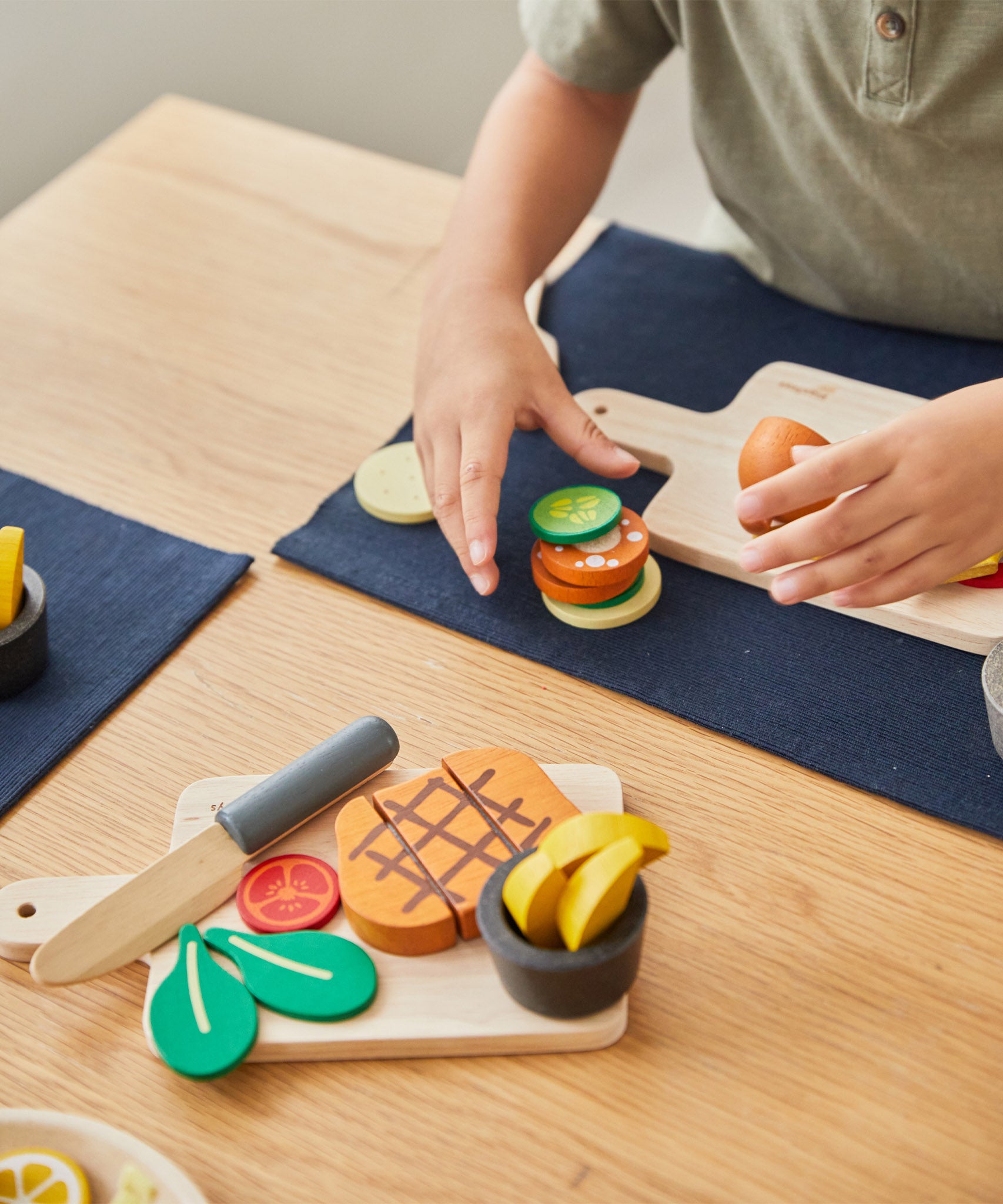 A close up of a child playing with the Plan Toys wooden steak set on the table. Set is available at Babipur.
