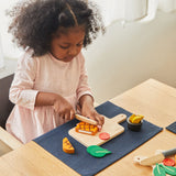 A girl sat by the table and playing with the Plan Toys wooden steak set available at Babipur.