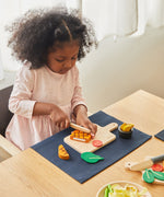 A girl sat by the table and playing with the Plan Toys wooden steak set available at Babipur.