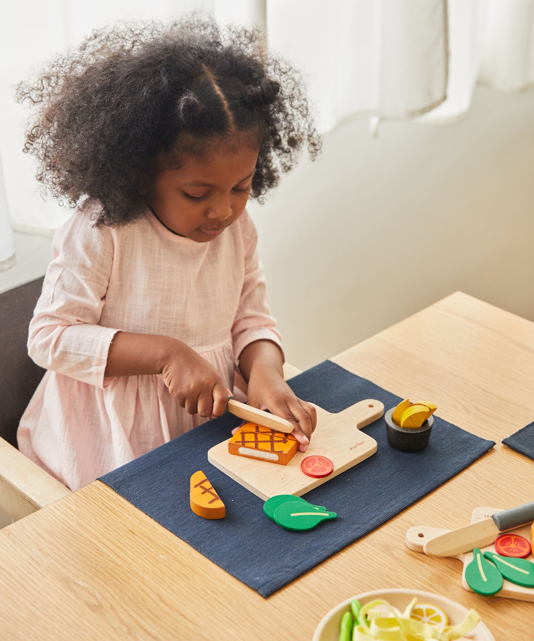 A girl sat by the table and playing with the Plan Toys wooden steak set available at Babipur.
