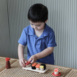 Child placing a pretend fish piece on rice from the PlanToys wooden sushi play set