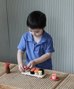 Child placing a pretend fish piece on rice from the PlanToys wooden sushi play set