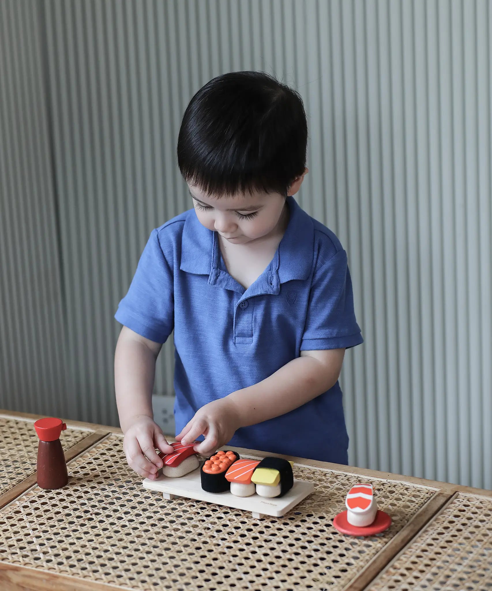 Child placing a pretend fish piece on rice from the PlanToys wooden sushi play set