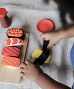 Child playing with the PlanToys wooden sushi play set on a white sheet