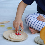 Child placing a pretend bacon piece on a waffle from the PlanToys wooden waffle play set.