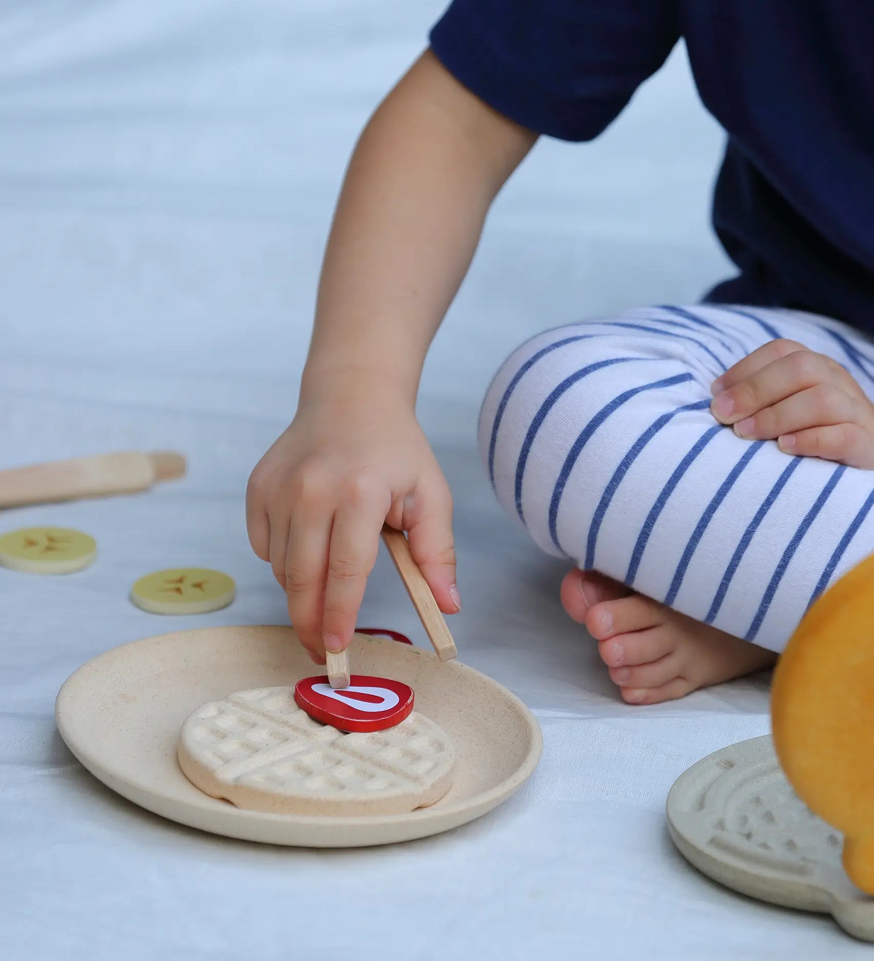 Child placing a pretend bacon piece on a waffle from the PlanToys wooden waffle play set.