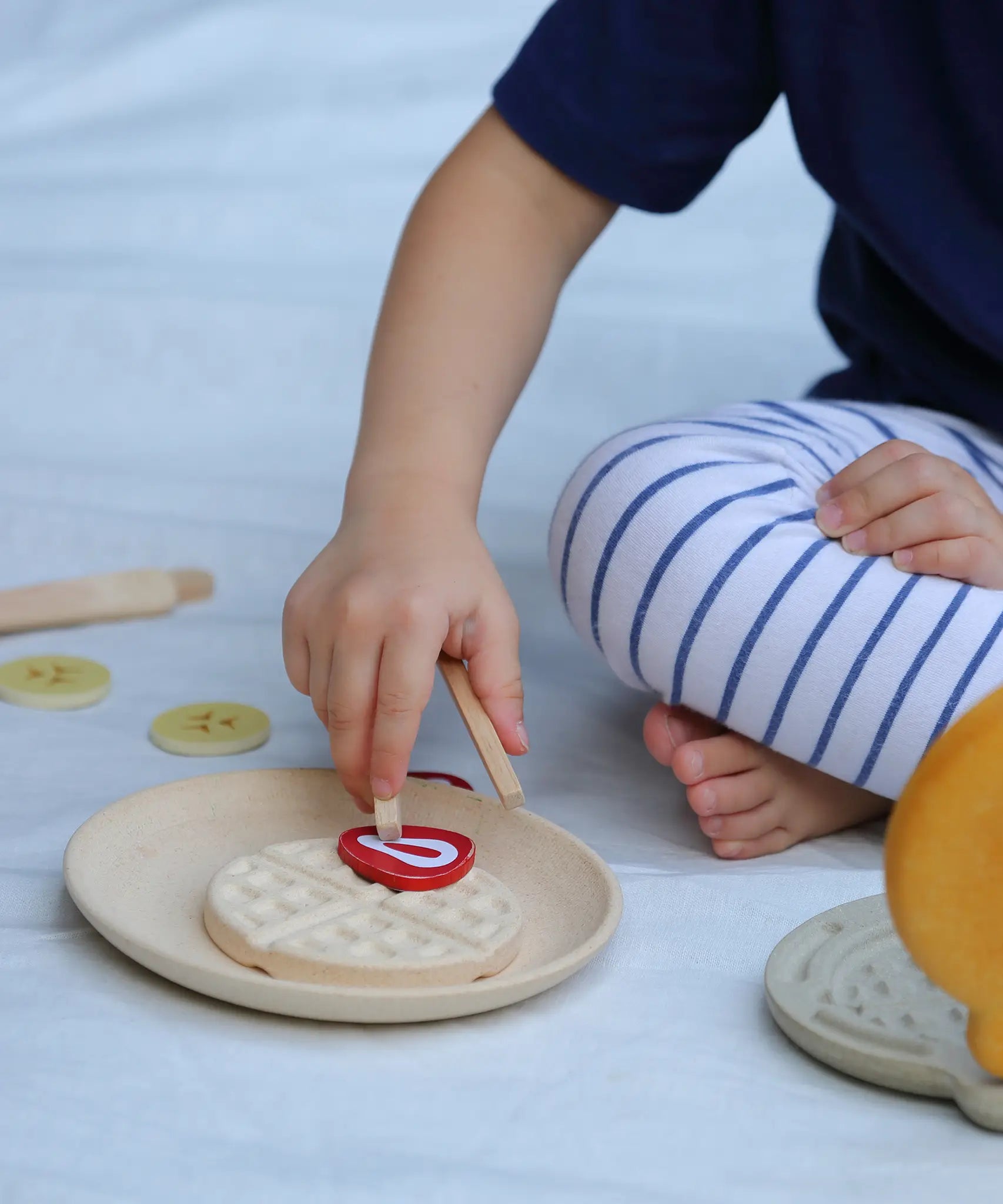 Child placing a pretend bacon piece on a waffle from the PlanToys wooden waffle play set.